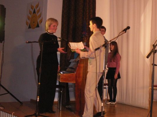 Renginio vedėjas Evaldas Račkauskas įteikia padėką Šiaulių rajono Naisių pagrindinės mokyklos mokytojai Daivai Remeikienei
